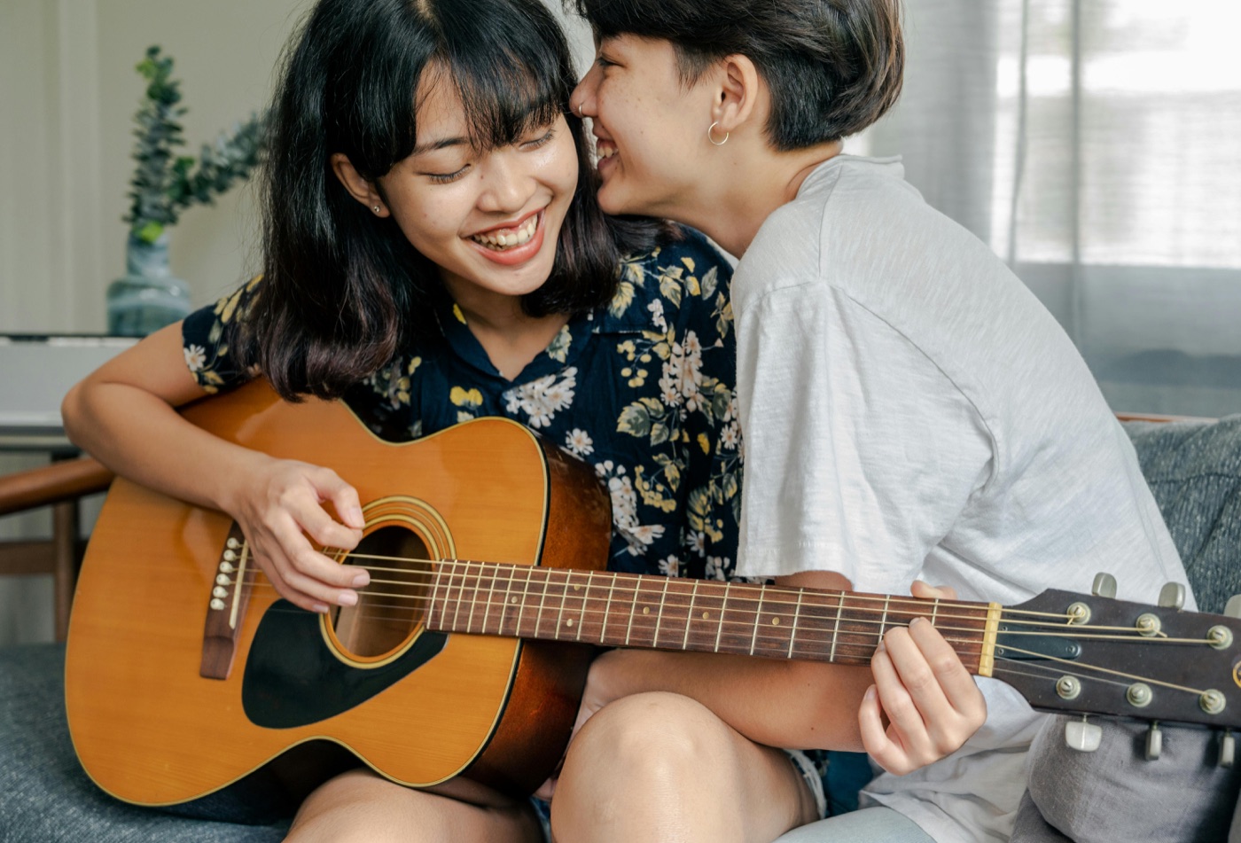 Two women in a tender moment at home, one playing guitar